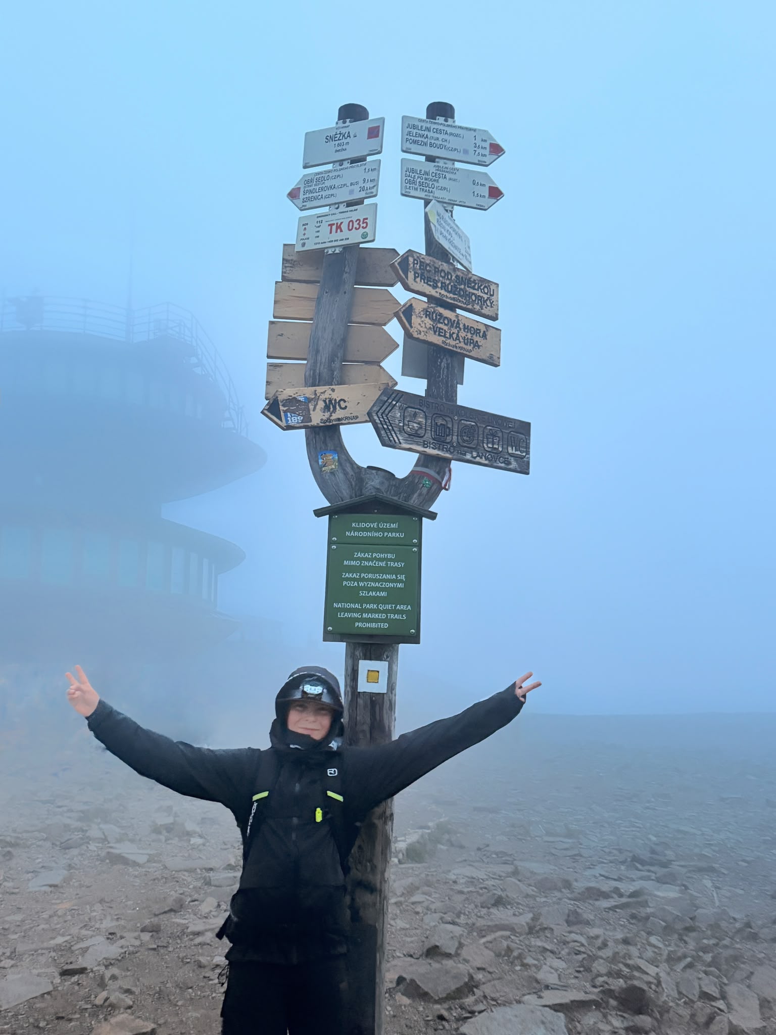 Tomášek u turistického rozcestníku na vrcholu Sněžky v husté mlze